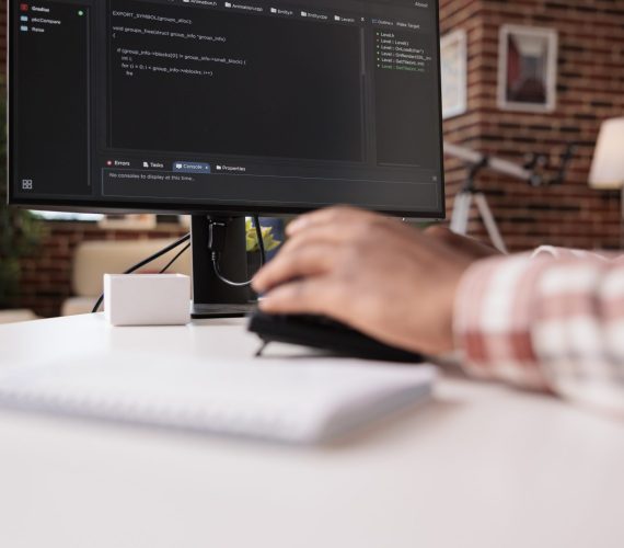 Selective focus on computer screen of african american programmer working remote from home developing software on pc. System developer writing code on personal computer typing algorithm on keyboard.